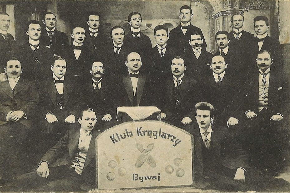 Fotografia przedstawiająca grupę mężczyzn. Przed nimi tablica z napisem klub kręglarzy bywaj.
