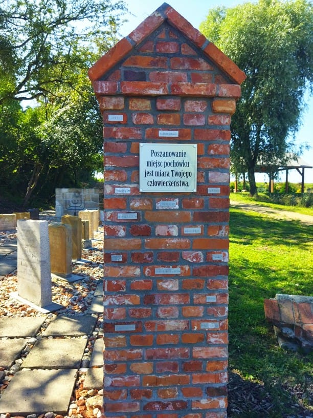 Murowany słup przy wejściu na teren lapidarium w Ryczywole. Na słupie tabliczka z napisem: Poszanowanie miejsc pochówku jest miarą twojego człowieństwa